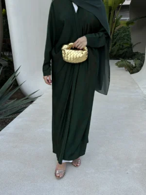 An elegantly standing woman wearing the Ula Emerald green Abaya