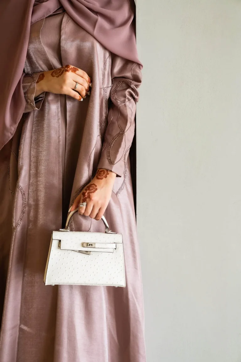 Close up of a A woman in a three-piece open abaya set holds a white handbag.