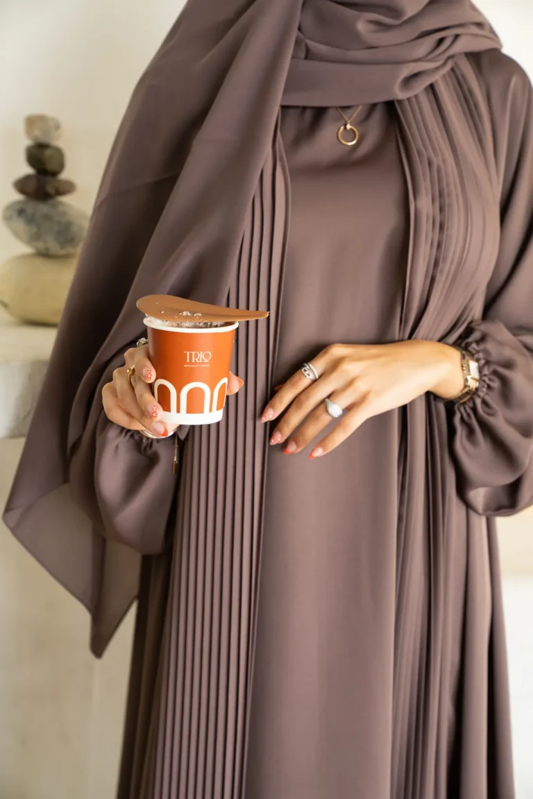 Stylish woman donning inner slip, pleated open brown abayah, and hijaab.