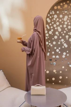 Woman enjoying a drink while wearing a mauve bisht abaya, showcasing its elegant design and intricate details.