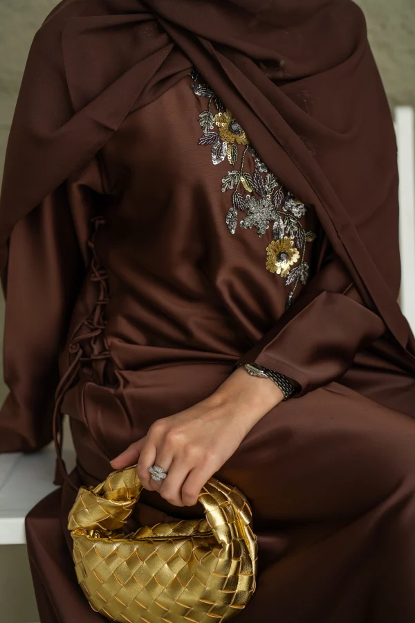 A model wearing a brown abaya set with a cinch on the side