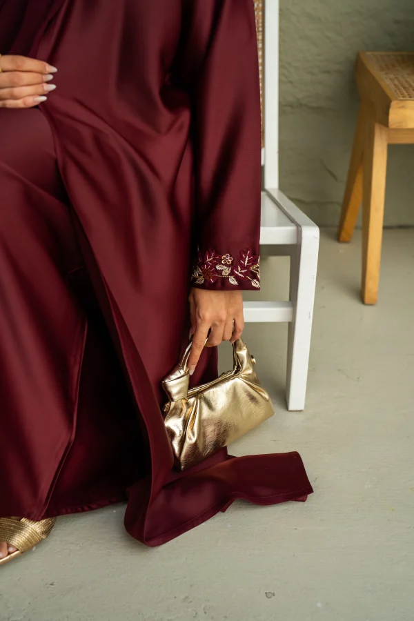 A model wearing maroon abaya dress posing with an handbag