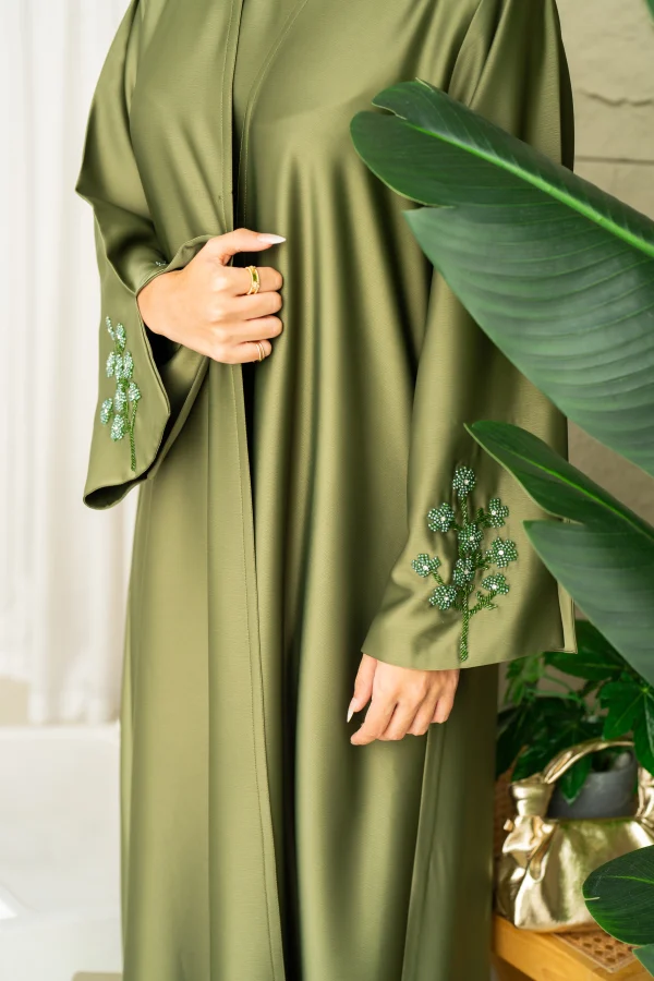 A model in an embellished green dress with matching sleeve