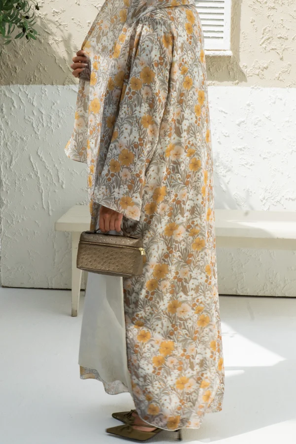 A model wearing a yellow chiffon abaya dress while holding a bag
